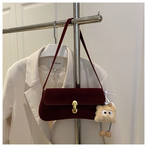 Detail of burgundy velvet baguette bag with gold buckle and plush charm on white blazer