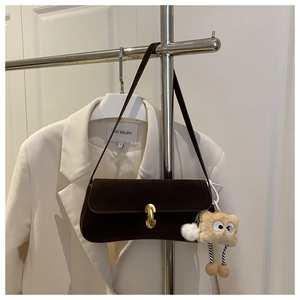 Detail of dark brown suede baguette bag with gold buckle and plush charm on white blazer