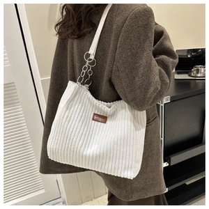 Close-up of white corduroy tote bag with brown leather tag and metal chain strap