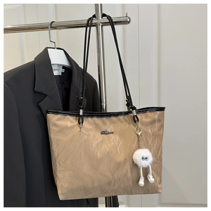 Detail of khaki pleated tote bag with black straps and a cute plush monster keychain
