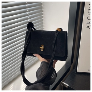 Detail of a black faux suede messenger bag with a golden turn-lock and knotted strap
