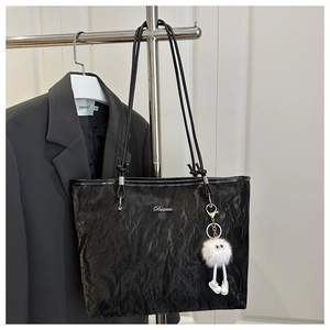 Close-up of black tote bag featuring unique wrinkled texture and a plush doll pendant