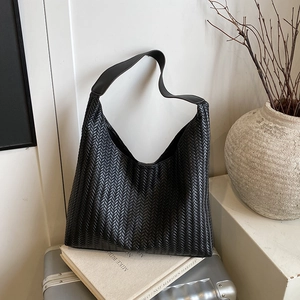 Classic black woven leather tote bag with wide strap displayed on a silver suitcase