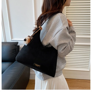 Détail du grand sac cabas noir en daim avec un pendentif en peluche chiot sur la bandoulière