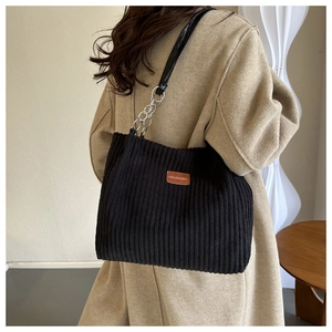 Close-up of black corduroy tote bag showing ribbed texture and leather chain strap