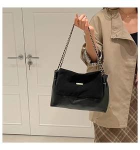 Detail of black chain shoulder bag featuring mixed leather texture and gold metal plate
