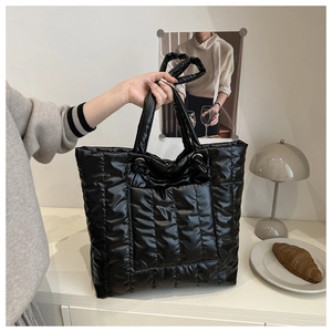 Detail of black quilted puffer tote bag with wide handles shown in a lifestyle setting