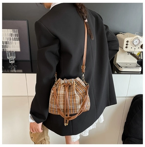 Detalle de un bolso cubo a cuadros marrones con cordón y correa en una modelo