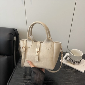Minimalist beige leather bucket bag with gold twist lock and adjustable shoulder strap