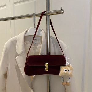 Burgundy velvet baguette shoulder bag with gold oval lock and plush charm on white blazer