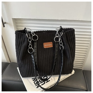 Detail of black corduroy tote bag showing metal chain strap and leather logo patch