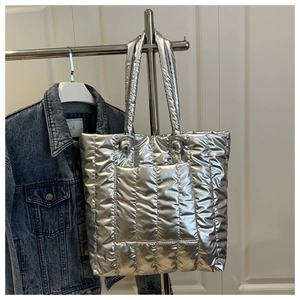 Detail of silver metallic quilted tote bag hanging on a rack with denim jacket style