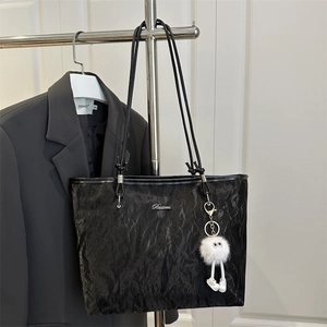 Black crinkle textured tote bag with long handles and a white plush monster keychain charm