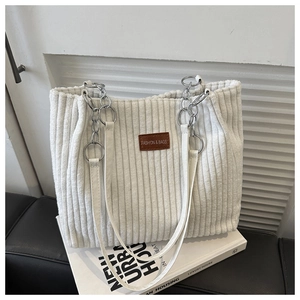 Detail of corduroy tote bag featuring a brown leather patch and chain shoulder strap