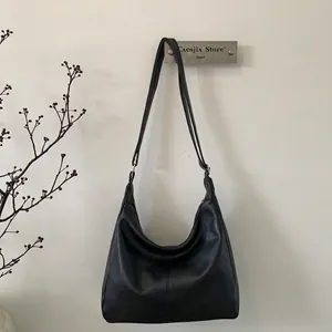 Minimalist black matte PU leather hobo tote bag with wide strap on a white wall