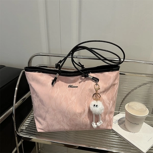 Large capacity pink tote bag with black straps and fuzzy eye charm on a metal shelf