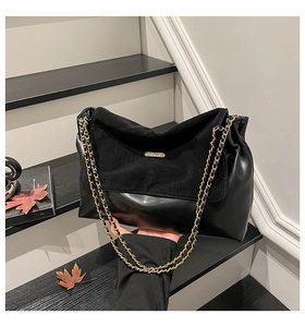 Detail of black patchwork leather shoulder bag with gold chain strap on stairs