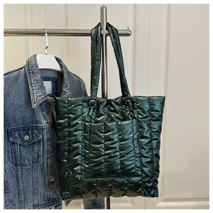 Detail of dark green quilted tote bag featuring metallic finish and vertical padding texture