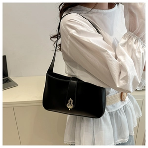 Close-up of black leather underarm bag with an artistic golden wavy metal buckle