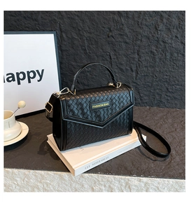 Detailed close-up of black woven leather handbag with gold hardware on white books