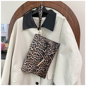 Détail de la pochette léopard avec barre dorée présentée sur un manteau chic