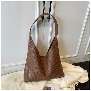Macro detail of the woven texture and wide leather strap on this brown hobo shoulder bag