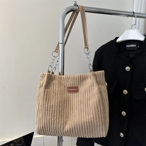 Large khaki corduroy tote bag with leather straps and silver chains hanging on metal stand