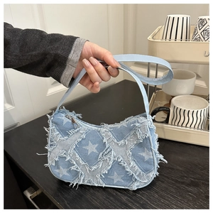 Detail of denim crossbody bag with frayed star patterns and a silver metal zipper