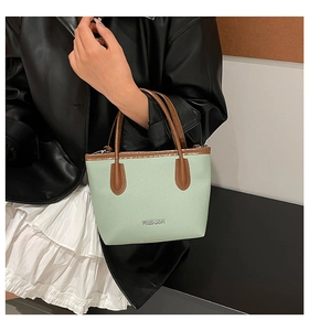 Detail of mint green leather texture and silver FASHION logo on minimalist handbag