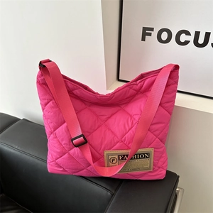 Pink quilted rhombus tote bag with adjustable strap displayed on a black leather sofa
