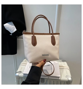 Close-up of litchi grain texture and metal FASHION logo on cream bucket bag