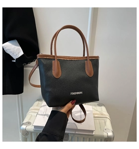 Close-up of black and brown leather tote bag with FASHION metal logo on white suitcase