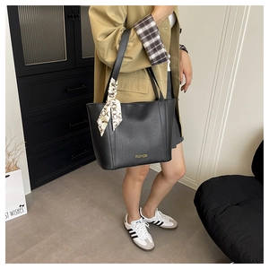 Dettaglio della borsa tote in pelle nera con scritte dorate e foulard in seta decorativo