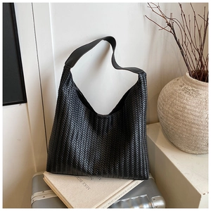 Detailed view of black woven leather hobo bag on books and silver luggage suitcase