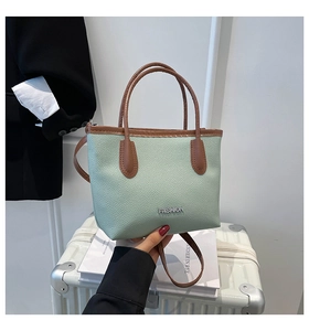 Detail of mint green tote with brown leather handles and silver FASHION logo