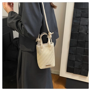 Close-up of cream woven crossbody bag showing textured herringbone pattern and knotted strap