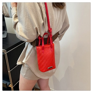 Close-up of red woven texture on crossbody bag with silver logo plate and knotted strap