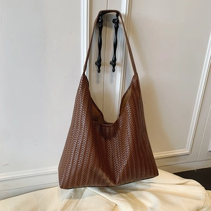 Dark brown woven leather hobo bag with V-shaped texture on a white decorative door