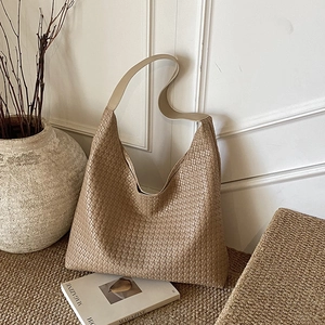 Khaki woven leather hobo bag with wide shoulder strap in a minimalist lifestyle setting