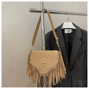 Close-up of khaki suede saddle bag featuring bohemian fringe and gold rivet details