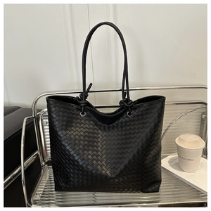 Detailed view of black woven leather tote bag with knotted straps on a modern shelf