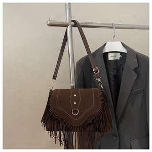 Detail of brown suede saddle bag featuring long fringes and gold metal ring hardware