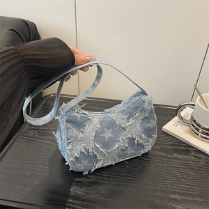 Blue denim crossbody bag with white stars and frayed edges on a dark wood table