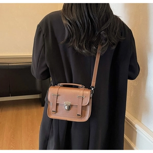 Detail of caramel brown satchel bag showing top handle and buckle on model
