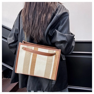 Detail of striped woven tote bag with brown leather trim and gold chain on a model