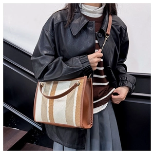 Detail of striped tote bag with brown leather trim and metal chain shoulder strap