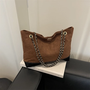 Brown quilted suede tote bag with chain strap and gold hardware on white pedestal