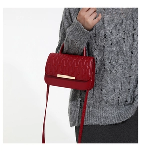 Detalle de bolso bandolera rojo acolchado con herrajes dorados en una modelo