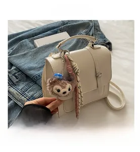 Close-up of cream faux leather handbag featuring woven rope charms and plush bear detail