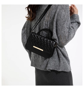 Detalle de bolso bandolera acolchado negro con hebilla dorada en una modelo
